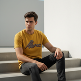 Man wearing mustard yellow HD print tee sitting on steps in minimalist outdoor space
