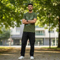 Man wearing olive green Rare Rabbit tee in outdoor green setting with sunlight